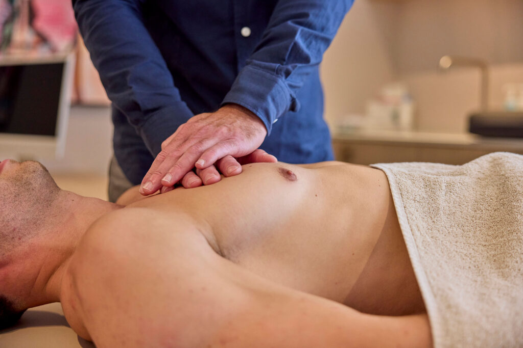 Osteopaat legt zijn handen op de borstkas van een man die op een behandeltafel ligt.